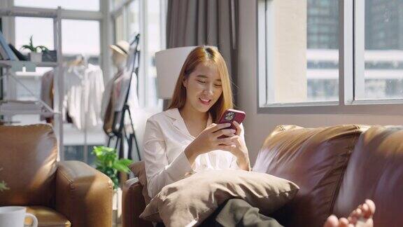 年轻的亚洲女人在沙发上用智能手机开心地笑着