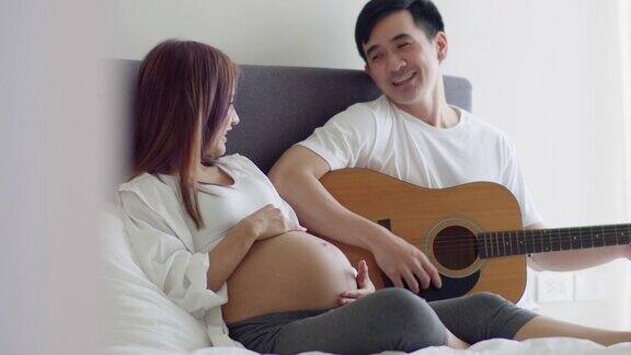 快乐的亚洲丈夫和怀孕的妻子花时间一起在卧室和丈夫弹吉他唱歌