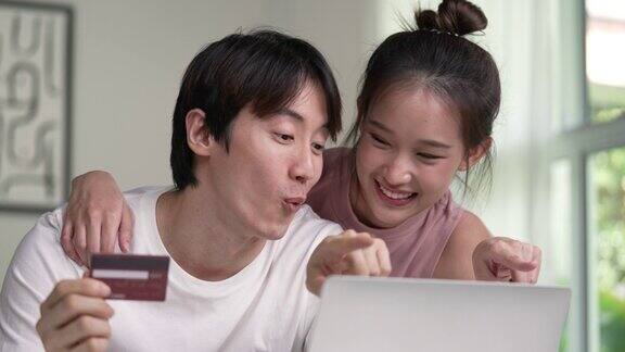 年轻的亚洲夫妇用信用卡和家里的笔记本电脑在网上购物年轻夫妇爱的时刻幸福观念