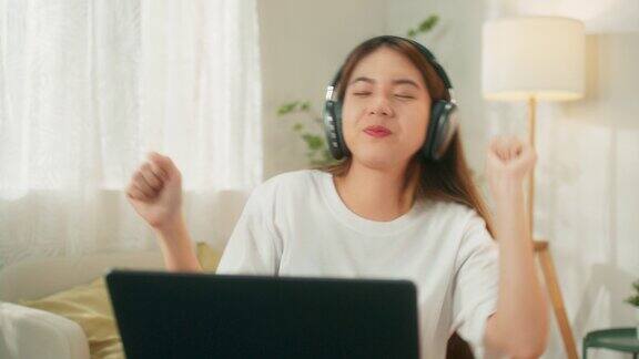 迷人的年轻亚洲女子跳舞无线耳机使用笔记本电脑听音乐