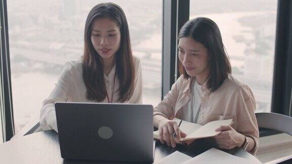 两个年轻貌美的亚洲女商人坐在办公室里在会议室里使用笔记本电脑