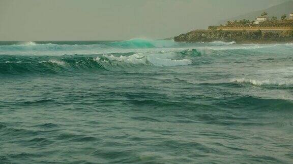 近景:海浪拍打在岩石沙滩上映衬着蓝天加那利群岛特内里费岛的自然景观