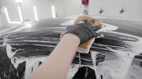 洗车工戴着橡胶手套用海绵和肥皂泡沫摩擦黑色汽车表面