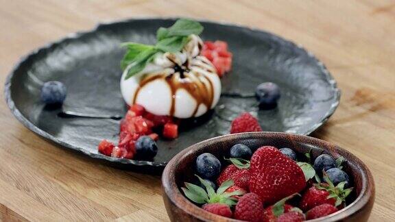 美味的早餐甜点布拉塔奶酪和新鲜浆果:草莓蓝莓覆盆子和薄荷叶在一个盘子在餐厅4k