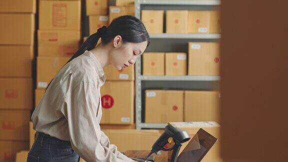 亚洲女性在网店仓库工作用条形码读卡器检查客户的包裹箱实现网上电商零售小生意的理念