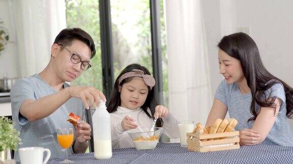 父母和女儿吃麦片牛奶早餐早上在厨房