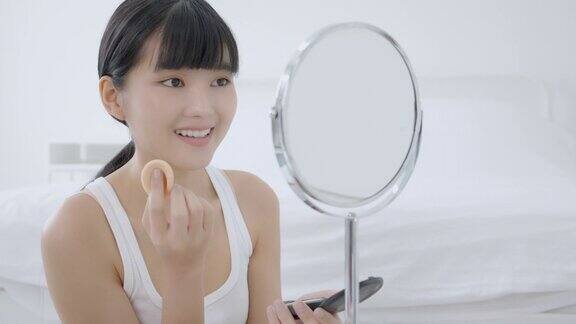 美丽年轻的亚洲女性在化妆镜的脸颊上涂粉扑卧室里有皮肤脸和皱纹的女孩美丽为女性美容护肤理念