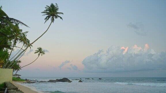 海洋景观与小泡沫波浪在热带度假胜地与沙滩和椰子树在天堂岛的地平线上橙色的夕阳和云在蓝色的波纹岩石水面上