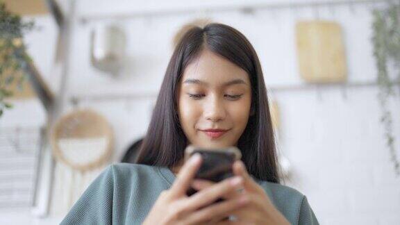快乐的年轻亚洲女人在家里放松亚洲女性站在厨房柜台使用手机