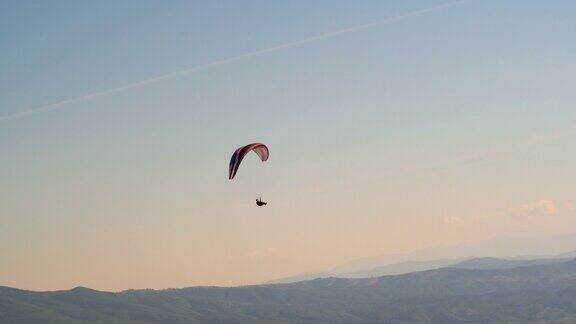 单人滑翔伞在山谷上空粉红色的夕阳天空下飞行极限运动空中滑翔伞