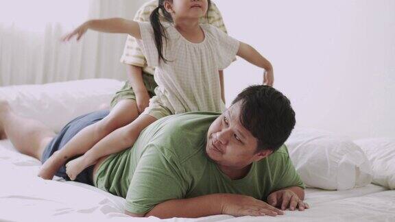 一家人在床上享受女儿在父亲背上玩耍