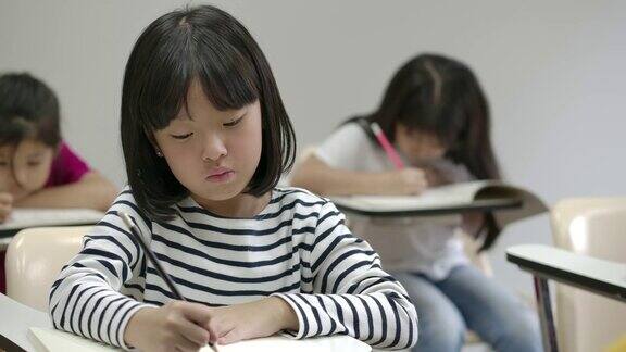 亚洲小女孩在笔记本上写字在教室里考试