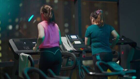 后视镜身体正面女人跑步跑步机与她的女性朋友在健身房在晚上面对城市的街灯