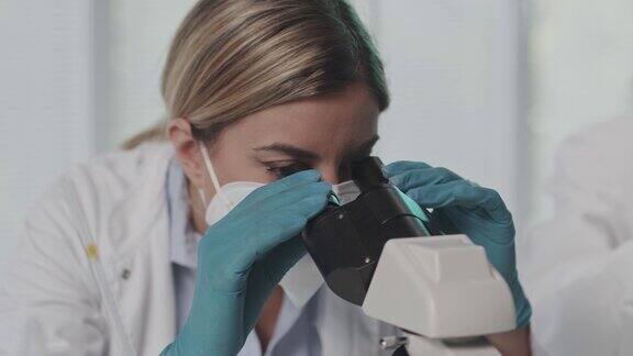 放大女性实验室技术人员在显微镜下分析样本的镜头