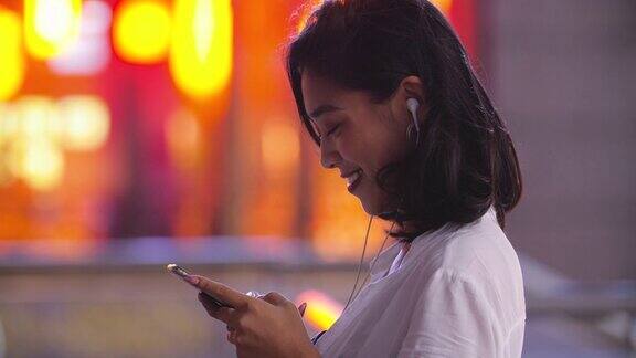 侧面的年轻亚洲妇女使用手机在街上