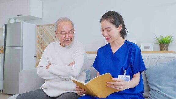 亚洲女性护理员在疗养院照顾老年男性年轻的女治疗师医生坐在沙发上读着快乐的书给年长成熟的男病人医疗保险服务理念