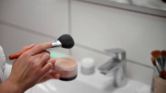 一个女人在浴室里拿着化妆刷涂着哑粉的特写镜头