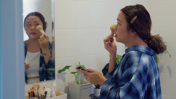 年轻的亚洲妇女在家里的浴室用粉刷刷上粉
