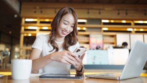 年轻的成年人快乐微笑的亚洲学生在线学习在网上聊天聊天会议使用智能手机在咖啡馆或办公室大学学院女生远程学习