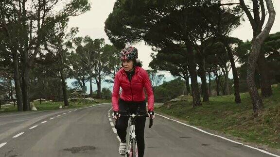 成熟的西班牙女性骑自行车在沿海公路上坡