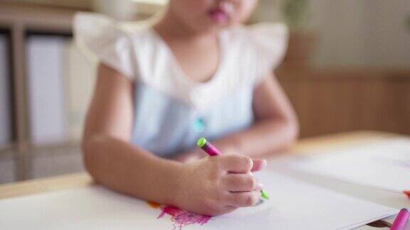 顽皮可爱的亚洲小女孩喜欢在家里的客厅用彩色蜡笔在纸上画画和着色孩子的技能发展和创造性活动在家学习艺术在周末