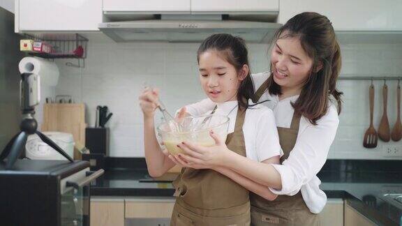 一名亚洲少女正在通过智能手机与老师在线学习做面包她的母亲帮助设置厨房的设备在家里