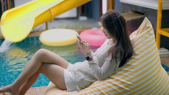 女子放松玩智能手机在泳池边