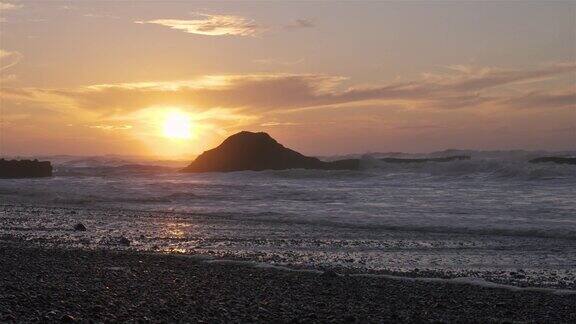 日出在空旷的岩石海滩与海浪背景后