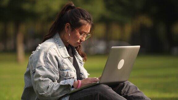 亚洲大学女孩忙着使用笔记本电脑在校园的草坪上