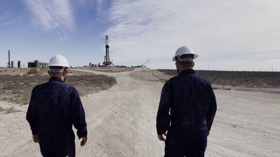 在德克萨斯州西部两名年轻的油田工人穿着防护装备、防火工作服和安全帽走向水力压裂石油和天然气钻井平台