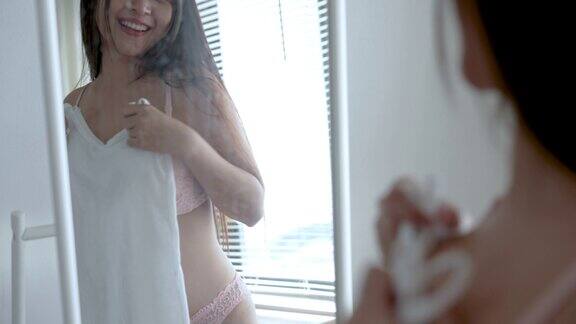 美丽的亚洲女人在衣架上挑选衣服然后在家里的卧室里看着镜子里的自己
