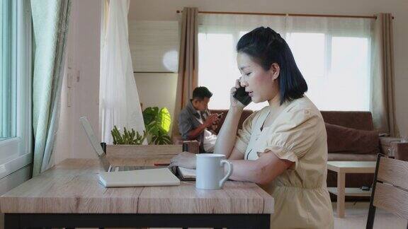 亚洲女学生在家里的客厅用笔记本电脑在线学习时打电话
