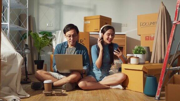 搬家休息放松亚洲结婚情侣夫妇在家里休息后一起用笔记本电脑唱歌搬家在新家的客厅里打包纸板箱搬家