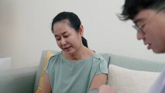 年轻的亚洲男性医生在为老年女性病人测量脉搏时使用血压计