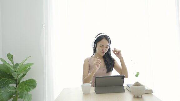 年轻的亚洲女子放松在沙发和听音乐与耳机在客厅在家里