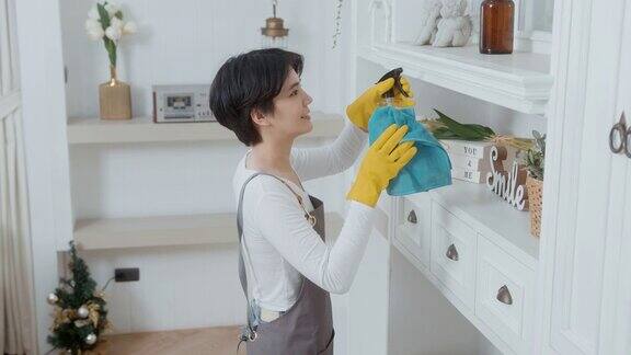 一名亚洲妇女戴着清洁手套用酒精喷雾消毒剂清洁房屋