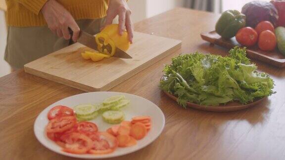 一个女人在砧板上切辣椒或甜椒的特写部分准备在家里做沙拉的食物