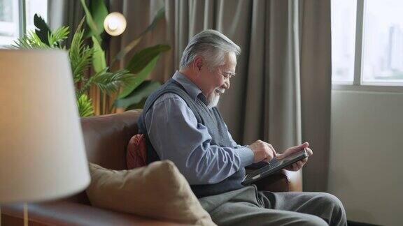 亚洲老人退休老人手使用平板电脑冲浪社交媒体浏览朋友在线社交交流距离连接幸福亚洲老人呆在家里使用平板电脑在家里