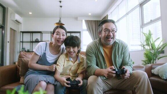 幸福快乐的亚洲家庭在家中一起玩电子游戏在隔离的时刻兴奋地手持操纵杆娱乐在家一家人微笑着一起坐在沙发上
