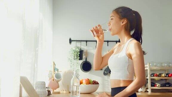 亚洲美女穿着运动服在家运动后喝水年轻的口渴活跃的运动女孩喝干净的矿物自然在杯子锻炼后保健在厨房在房子