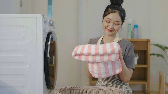 闻一闻笑一笑年轻的亚洲女人在家里用洗衣机洗衣服快乐的女孩和一个家庭清洁工闻到毛巾或衣服从洗涤幸福和家务