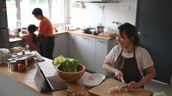 亚洲华人母亲在厨房柜台准备食物并使用数字平板电脑通过互联网学习