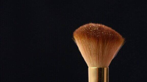 在黑色背景上从化妆刷上扫出金色闪光粉