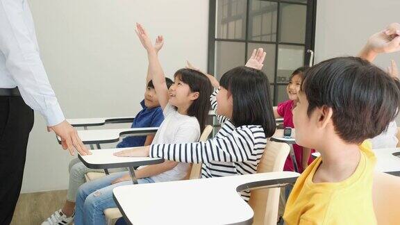 亚洲老师在学校的教室里教孩子们小男孩和小女孩一起举手接受评论教育理念、经验学习和技能发展