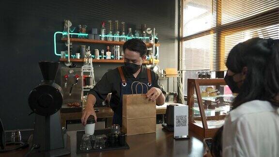 4K亚洲男子咖啡师戴着口罩用非接触式付款为顾客点外卖