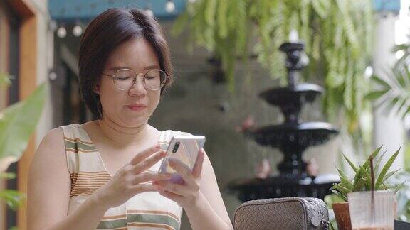 短发的女游客戴着眼镜坐在咖啡厅里用触摸智能手机在网上购物和社交媒体上搜索旅游信息长周末的活动让女性感到放松和快乐
