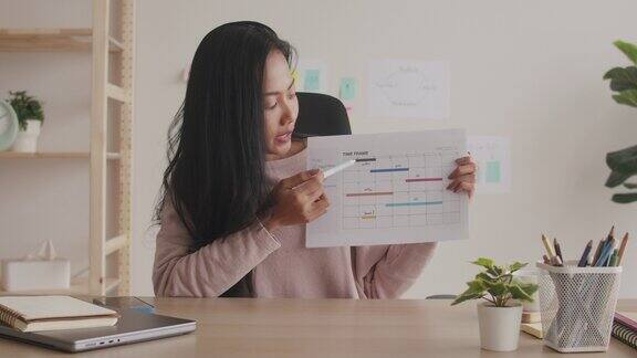 一位亚洲女商人在家工作时通过视频会议向同事展示一个图形用户界面原型