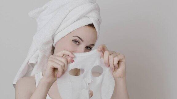 年轻女子头上戴着毛巾脸上拿着化妆用的面膜