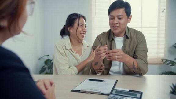女销售员保持房子的钥匙年轻的亚洲夫妇与休闲坐在桌子上感觉幸福的新房屋合同协议在房地产办公室
