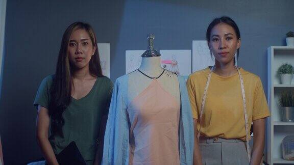 两位专业的亚洲女性时尚设计师自信地与休闲握着数码平板电脑自信地看着相机在商店的夜晚成功夫人裁缝骄傲的开始新的生意布店